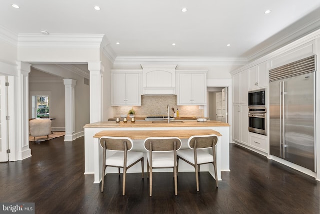 kitchen featuring wood counters, built in appliances, white cabinets, and an island with sink