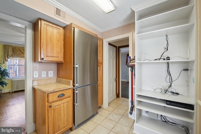 kitchen with light hardwood / wood-style floors, stainless steel refrigerator, radiator, ornamental molding, and a textured ceiling