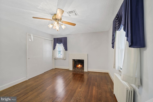 unfurnished living room with a brick fireplace, radiator, a textured ceiling, and dark wood-type flooring