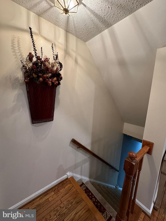 staircase featuring hardwood / wood-style floors, a textured ceiling, and vaulted ceiling