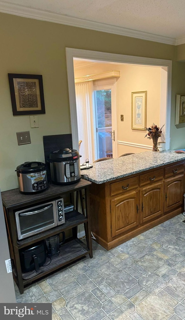 kitchen with a textured ceiling, light stone counters, and crown molding