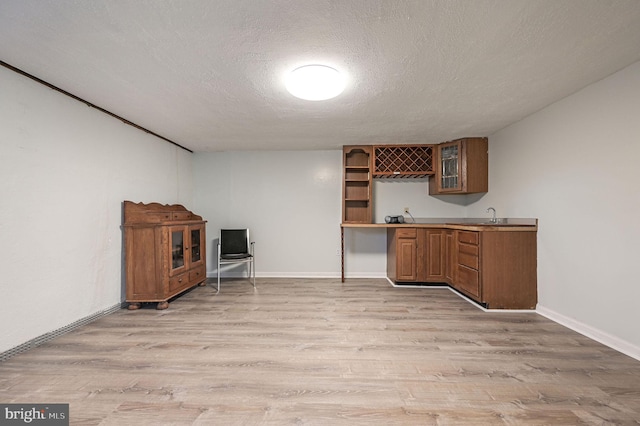 bar with a textured ceiling, light hardwood / wood-style floors, and sink