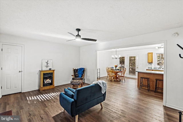 living room featuring ceiling fan with notable chandelier, a fireplace, a textured ceiling, and dark hardwood / wood-style floors