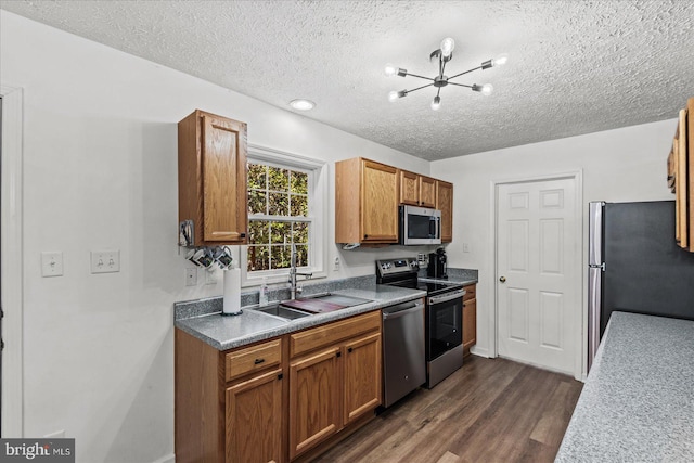 kitchen with appliances with stainless steel finishes, a textured ceiling, a chandelier, dark wood-type flooring, and sink