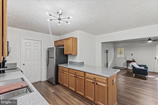 kitchen featuring dark wood-type flooring, kitchen peninsula, a textured ceiling, ceiling fan with notable chandelier, and stainless steel refrigerator