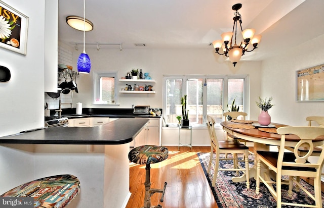 kitchen with kitchen peninsula, hanging light fixtures, white cabinetry, a chandelier, and light hardwood / wood-style flooring