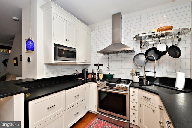 kitchen featuring wall chimney exhaust hood, tasteful backsplash, appliances with stainless steel finishes, and white cabinetry