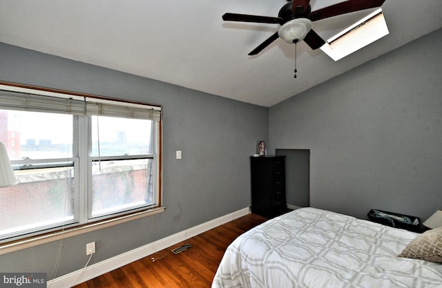 bedroom with dark wood-type flooring, vaulted ceiling with skylight, and ceiling fan