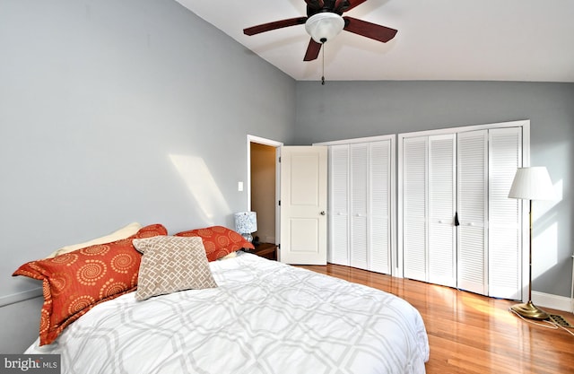 bedroom with vaulted ceiling, ceiling fan, hardwood / wood-style floors, and two closets