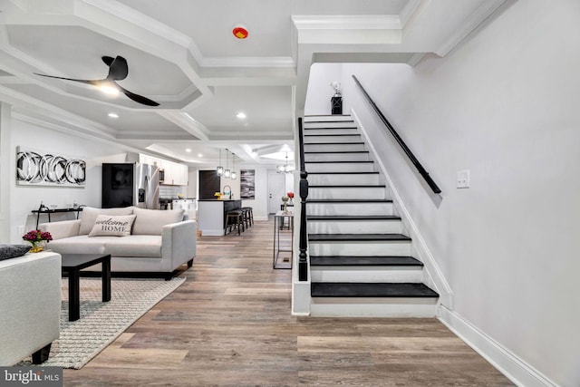 staircase with ceiling fan with notable chandelier, crown molding, coffered ceiling, and hardwood / wood-style floors