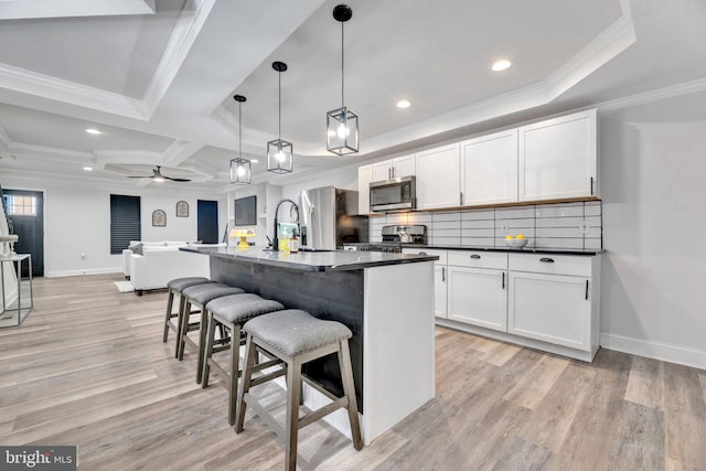 kitchen featuring light hardwood / wood-style floors, pendant lighting, crown molding, an island with sink, and appliances with stainless steel finishes