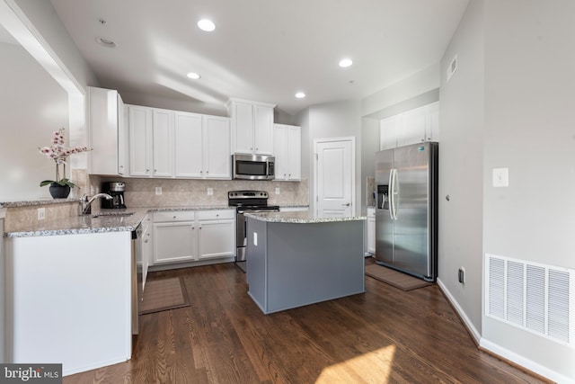 kitchen featuring dark wood-type flooring, white cabinets, light stone countertops, appliances with stainless steel finishes, and a kitchen island