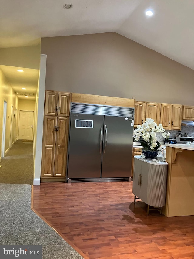 kitchen with vaulted ceiling, tasteful backsplash, stainless steel built in refrigerator, stove, and dark wood-type flooring