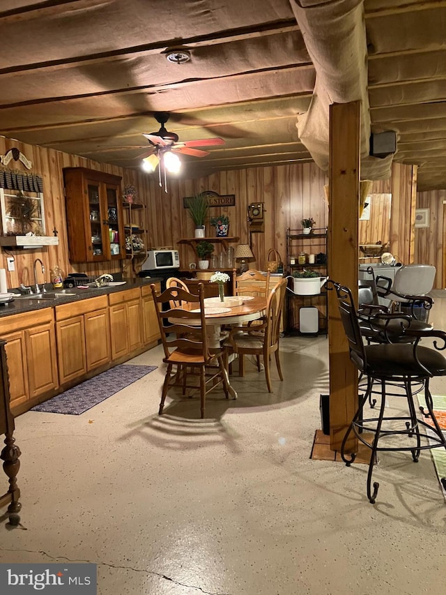 dining area with ceiling fan, sink, and wooden walls