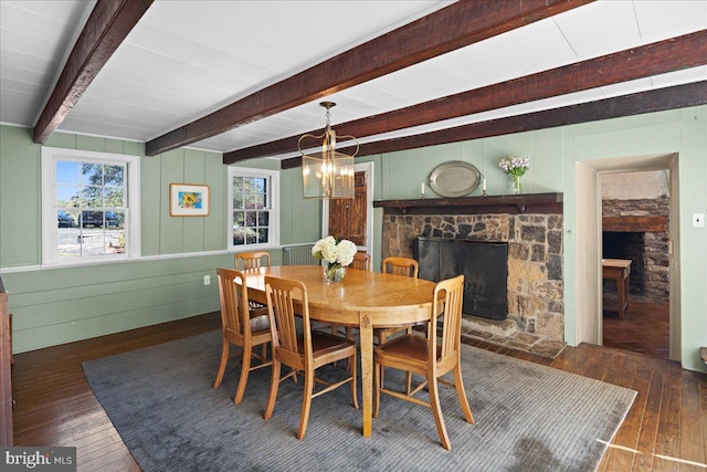 dining room featuring a stone fireplace, a notable chandelier, dark hardwood / wood-style floors, and beamed ceiling