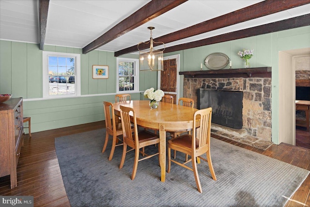 dining area featuring a stone fireplace, a notable chandelier, beamed ceiling, and dark hardwood / wood-style flooring