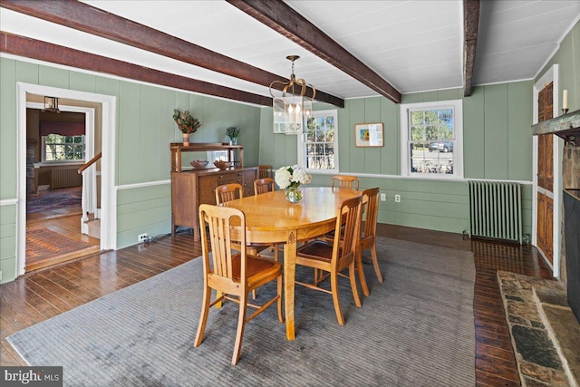 dining area featuring radiator, beam ceiling, dark wood-type flooring, wooden walls, and a notable chandelier