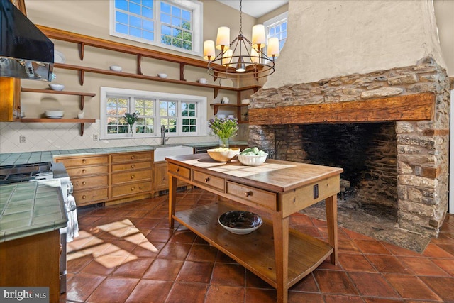 kitchen featuring decorative backsplash, hanging light fixtures, ventilation hood, a notable chandelier, and a towering ceiling