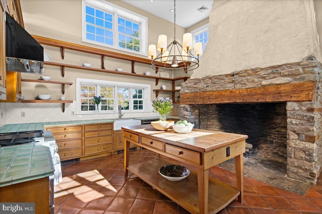 kitchen with sink, backsplash, hanging light fixtures, exhaust hood, and a chandelier