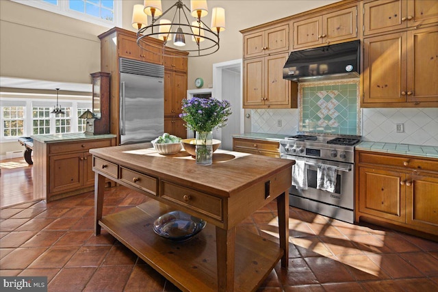 kitchen featuring tasteful backsplash, dark tile patterned floors, hanging light fixtures, and high end appliances