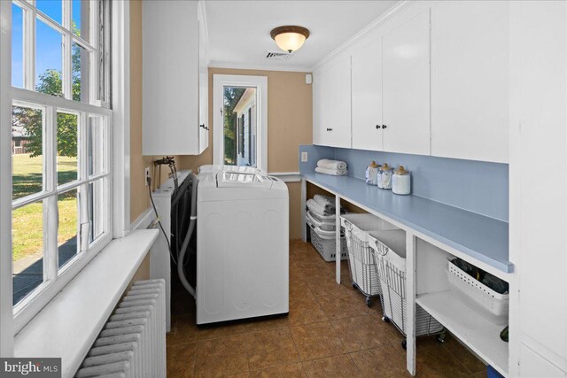 laundry room with dark tile patterned flooring, radiator heating unit, ornamental molding, cabinets, and washing machine and clothes dryer