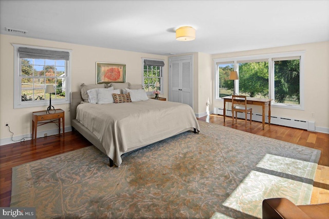 bedroom with dark wood-type flooring, multiple windows, and a baseboard heating unit