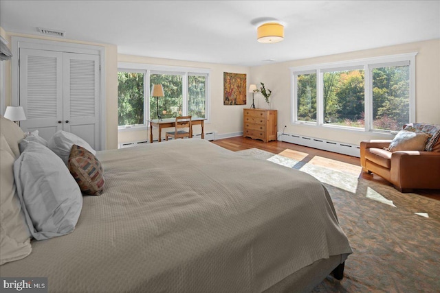 bedroom featuring a baseboard heating unit, light wood-type flooring, and a closet