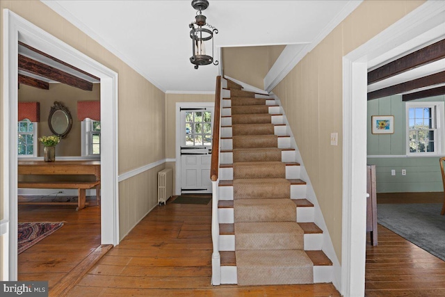 stairway with crown molding, wood-type flooring, radiator heating unit, and plenty of natural light