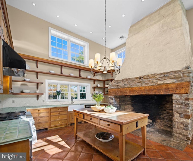 kitchen with dark tile patterned flooring, exhaust hood, backsplash, sink, and decorative light fixtures