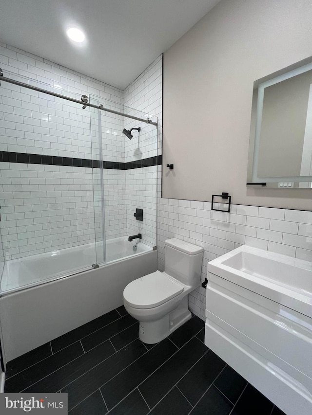 full bathroom featuring tile walls, vanity, combined bath / shower with glass door, tile patterned flooring, and toilet