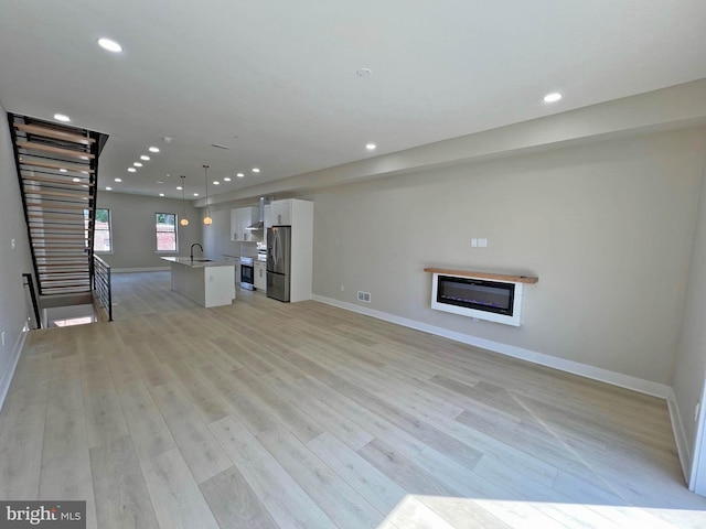 unfurnished living room with light hardwood / wood-style flooring and sink