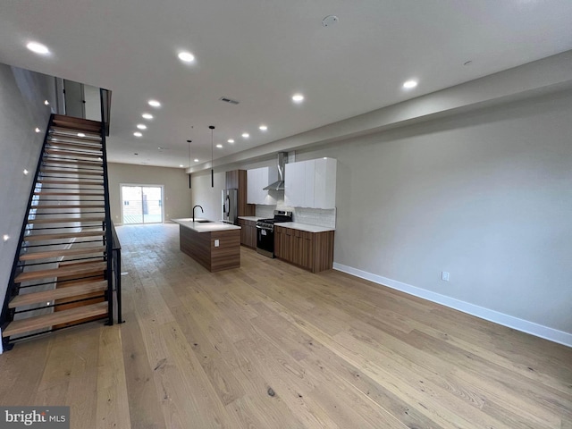 kitchen with pendant lighting, light wood-type flooring, white cabinets, stainless steel appliances, and a center island with sink