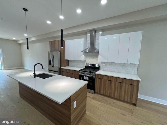 kitchen with an island with sink, white cabinets, appliances with stainless steel finishes, and wall chimney range hood