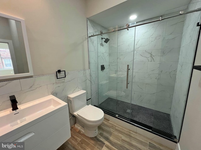 bathroom featuring tile walls, hardwood / wood-style flooring, a shower with door, vanity, and toilet