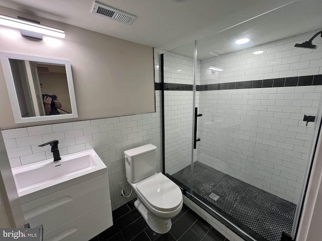 bathroom with tile walls, a shower with door, tile patterned floors, vanity, and toilet