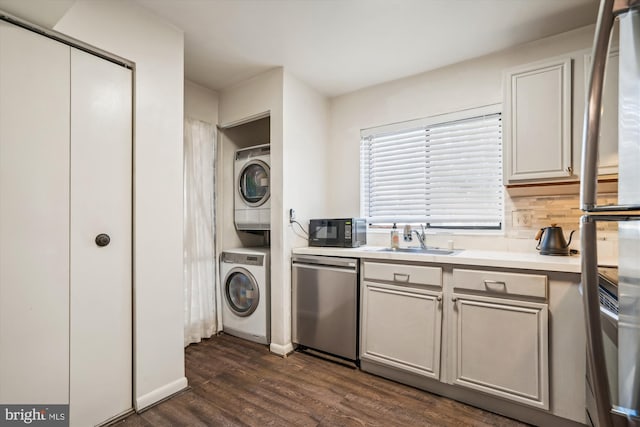 kitchen with sink, appliances with stainless steel finishes, stacked washer and clothes dryer, and dark wood-type flooring