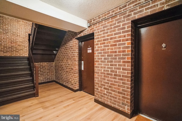 hall featuring light hardwood / wood-style floors, a textured ceiling, and brick wall