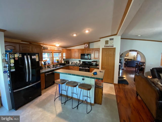 kitchen featuring vaulted ceiling, a breakfast bar, black appliances, a center island, and sink