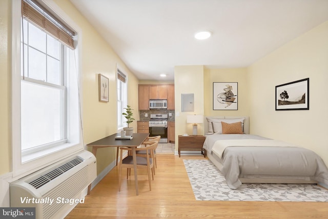 bedroom with electric panel, a wall unit AC, and light hardwood / wood-style floors