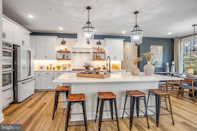 kitchen featuring custom exhaust hood, white cabinets, stainless steel appliances, and an inviting chandelier