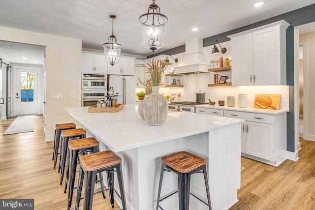 kitchen with custom range hood, a kitchen island with sink, and white cabinets