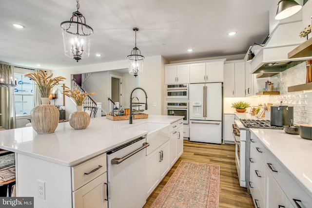 kitchen featuring white cabinets, a center island with sink, light wood-type flooring, decorative light fixtures, and high end appliances