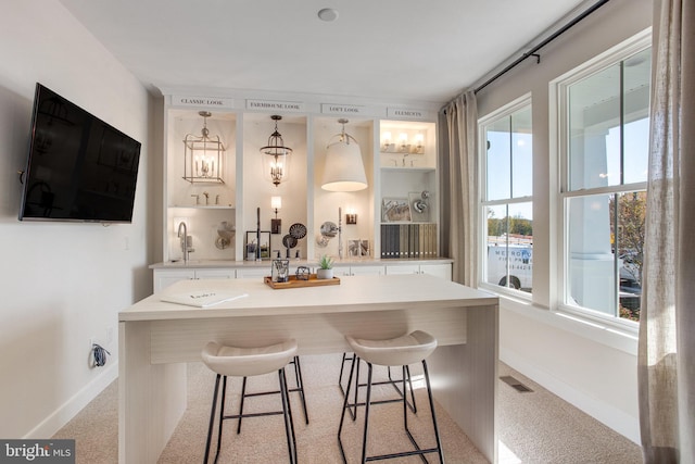 bar with light carpet, white cabinetry, and decorative light fixtures