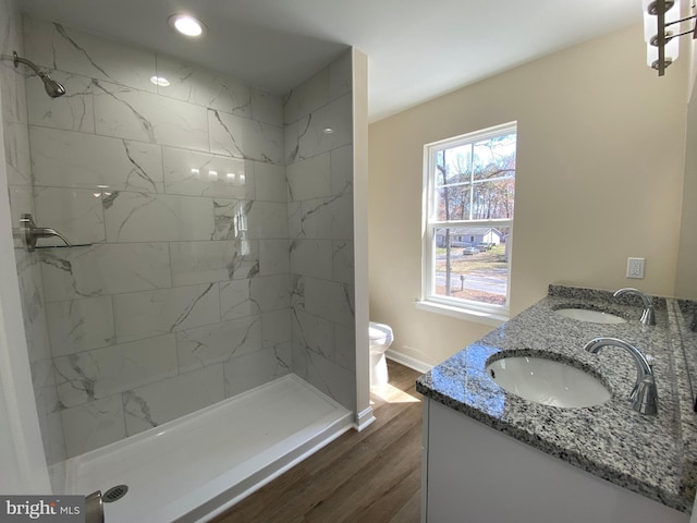 full bath with a sink, a tile shower, double vanity, and wood finished floors
