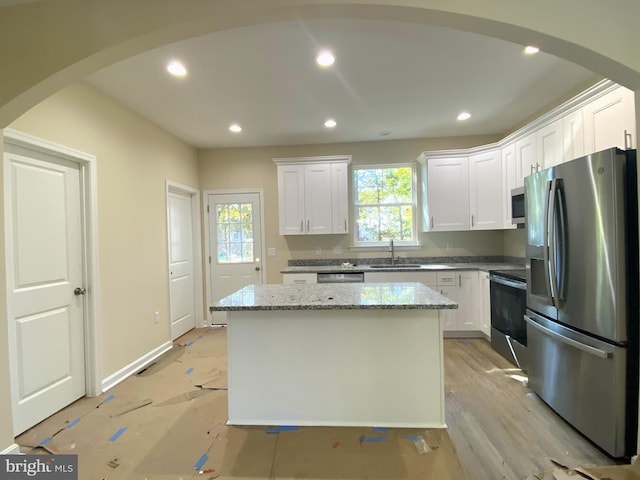 kitchen featuring a kitchen island, sink, light stone counters, appliances with stainless steel finishes, and white cabinetry