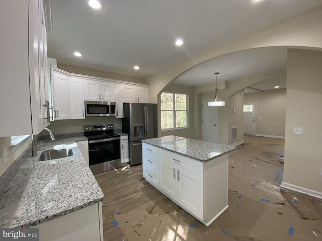 kitchen with sink, a kitchen island, white cabinetry, appliances with stainless steel finishes, and light stone countertops