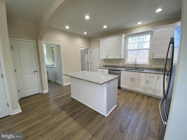 kitchen featuring stainless steel dishwasher, dark wood finished floors, white cabinets, a kitchen island, and a sink