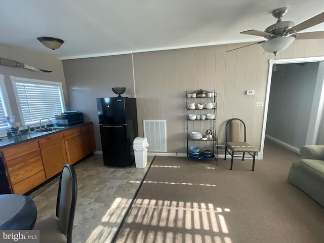 kitchen featuring wood walls, sink, ceiling fan, and black fridge