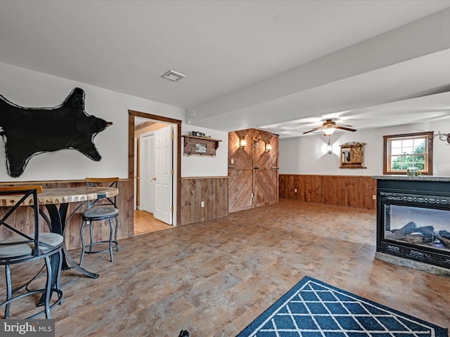 living room with a multi sided fireplace, wooden walls, and ceiling fan