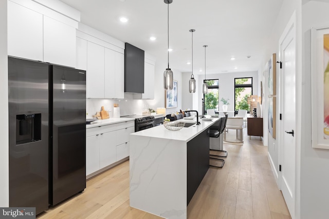 kitchen with light hardwood / wood-style floors, a kitchen island with sink, white cabinetry, stainless steel appliances, and decorative light fixtures